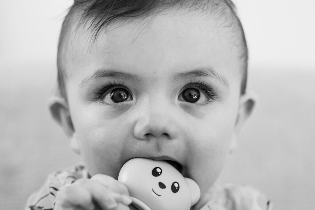 Baby chewing on a teething toy in a black and white portrait