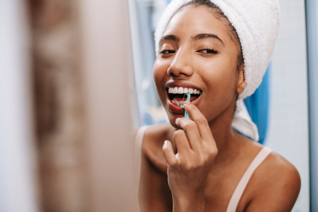 Smiling woman flossing her teeth with a floss pick