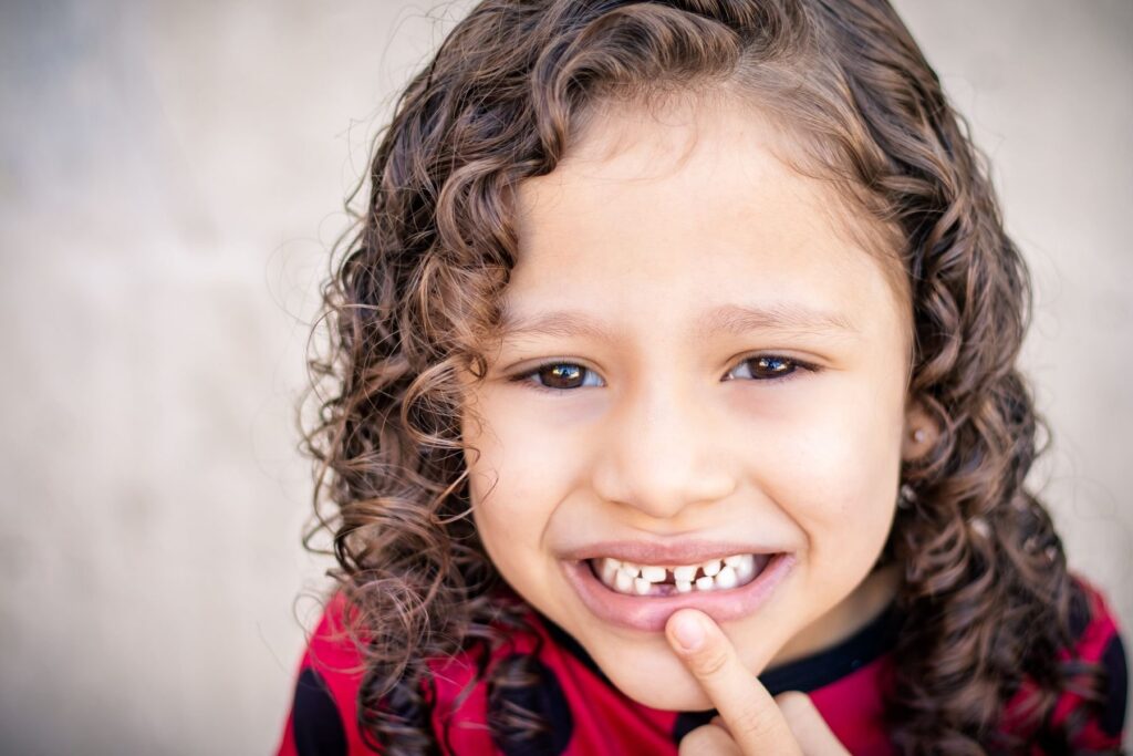 Smiling child with curly hair showing a missing front tooth
